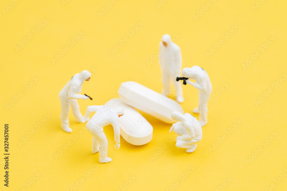 Miniature people doctors with protective suit and mask research on white pills tablet medicine on yellow background, Corona virus, COVID-19 flu medicine or virus vaccine medical research concept Miniature people doctors with protective suit and mask research on white pills tablet medicine on yellow background, Corona virus, COVID-19 flu medicine or virus vaccine medical research concept