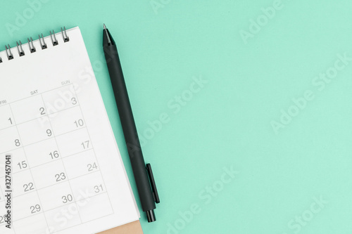 Flat lay or top view of white clean calendar with black pen on pastel green background with copy space, schedule or project milestone and reminder, business meeting planning concept