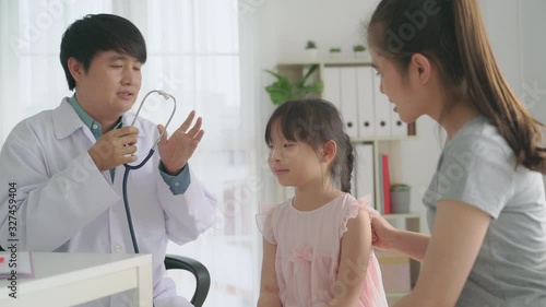 Smiling asian man doctor pediatrician holding stethoscope examining listening kid girl checking up preschool patient visit pediatrician with mom
