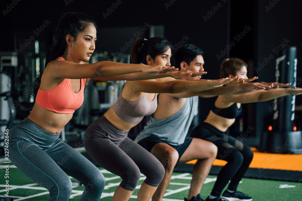 Close-up of group of athletic young Asian people in sportswear doing squat and exercising at the gym. Intense workout and healthy lifestyle concept Close-up of group of athletic young Asian people in sportswear doing squat and exercising at the gym. Intense workout and healthy lifestyle concept