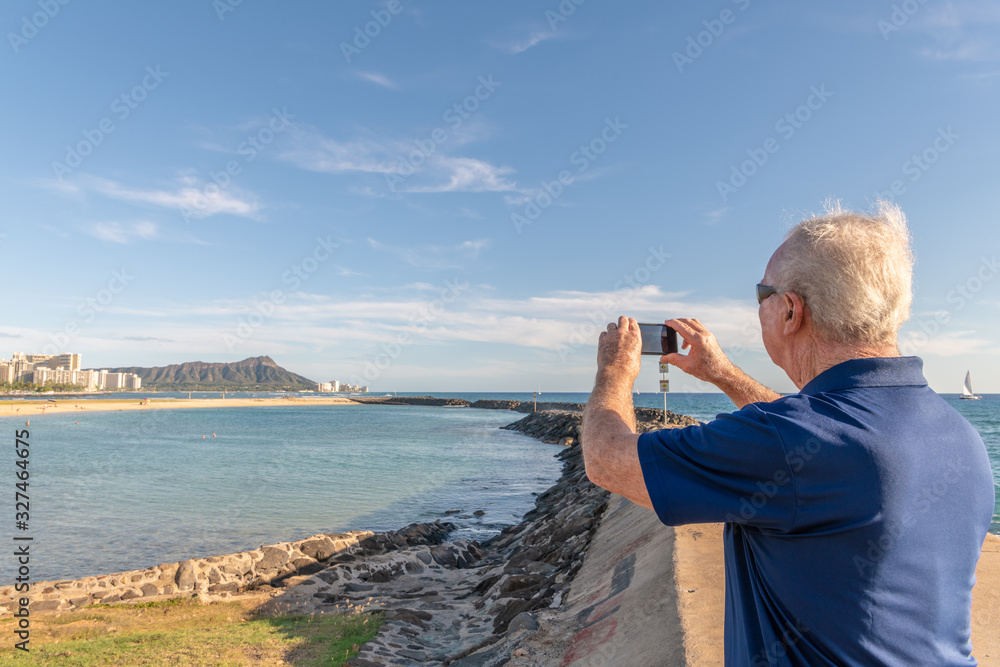 A senior man takes a photo of Diamond Head while on a family trip to Honolulu, Hawaii.