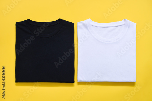 top view of folded black and white color t-shirt on yellow background, copy space, flat lay