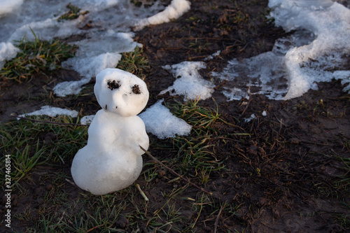 Last miniature snowman standing in mud and grass, melting in the evening sun in spring