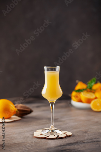 Limoncello in glass, sweet Italian lemon liqueur, traditional strong alcoholic drink and lemons on the blue background.