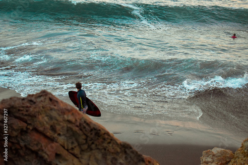 Valokuva Hombre camina y observa las olas mientras sostiene su tabla de surf