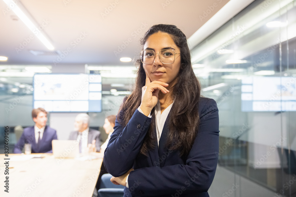 Thoughtful woman holding hand on chin and looking at camera. Serious businesswoman in eyeglasses searching solution. Business concept Thoughtful woman holding hand on chin and looking at camera. Serious businesswoman in eyeglasses searching solution. Business concept