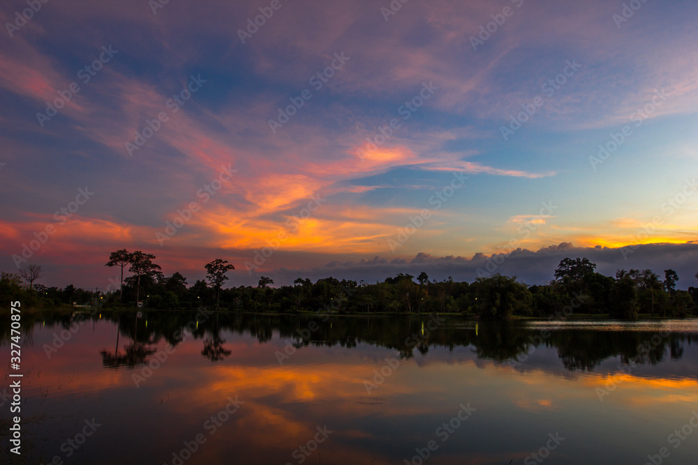 Fototapeta premium Wallpaper blurred nature of the twilight light in the evening by the large water basin surrounded by big trees, the integrity of the forest