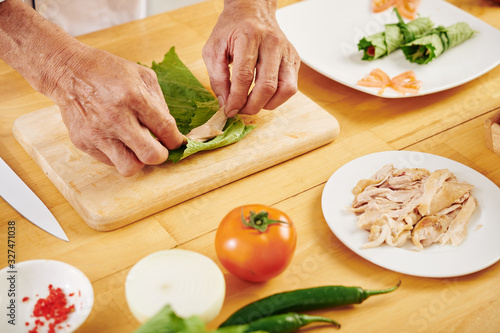 Hands of man wrapping pieces of chicken fillet in lettuce leaves when cooking healthy appetizers