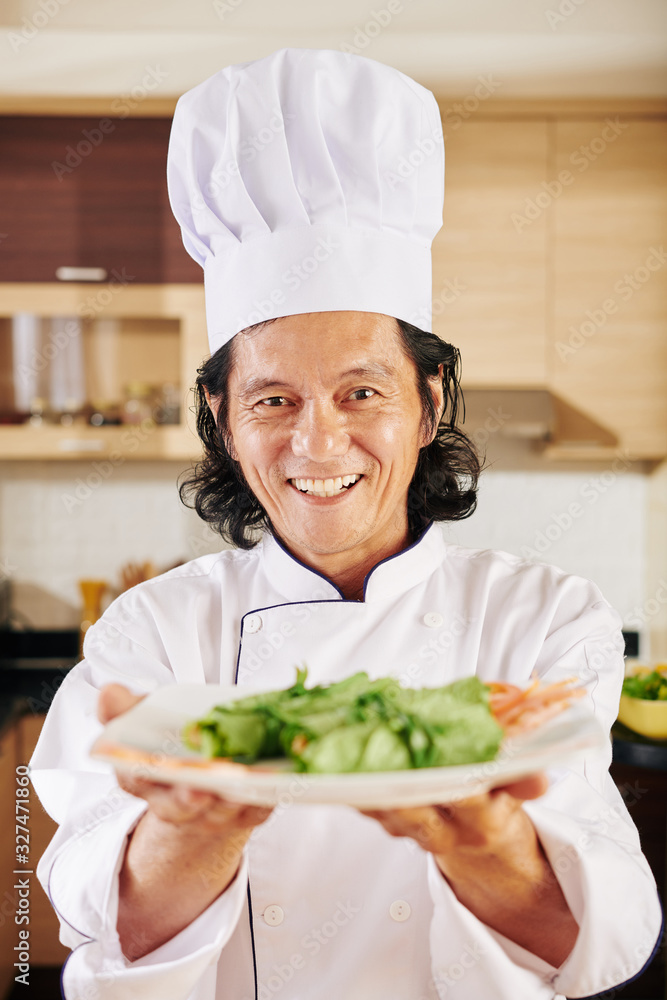 Portrait of positive Asian man offering you a plate of tasty delicious salad Portrait of positive Asian man offering you a plate of tasty delicious salad