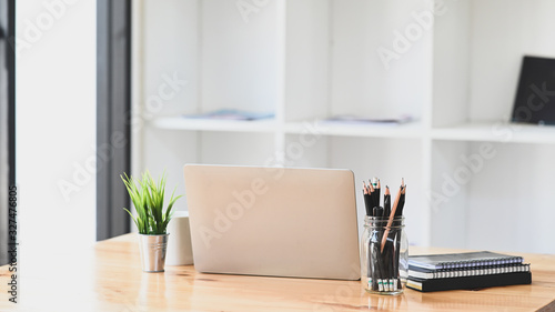 Computer laptop  Pencil holder  Potted plant  Notebook and coffee cup putting together on modern wooden table with office book shelf as background.