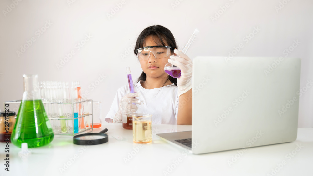 Photo of adorable schoolgirl doing a scientific experiment at the modern white table with chemistry glassware over the white laboratory wall as background. Education for kids concept. Photo of adorable schoolgirl doing a scientific experiment at the modern white table with chemistry glassware over the white laboratory wall as background. Education for kids concept.