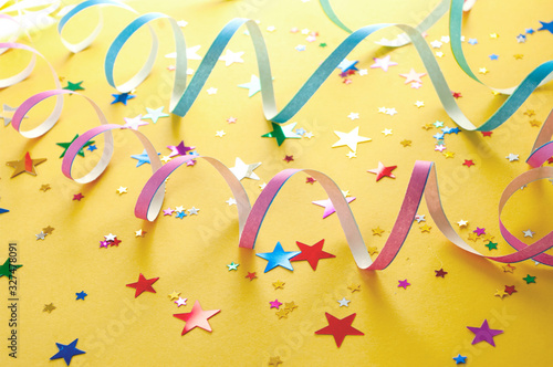 Colorful carnival serpentines and party confetti stars on yellow background.