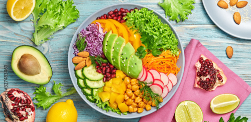 Buddha bowl salad with avocado, tomato, lettuce, cucumber, red cabbage, chickpeas, pomegranate. Paleo diet, healthy vegan and balanced food concept. Fresh rainbow mix green salad on wood, flat lay