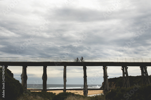 silhouette photos of bicycle riders on Kilcunda Bourne Creek Trestle Bridge on an overcast day in Gippsland Victoria with the sea in the background photo