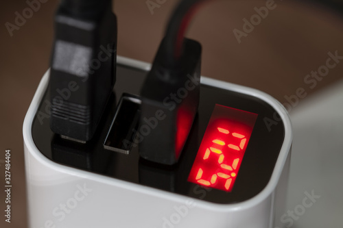 Mobile devices are charging from socket charger for three USB ports output with voltage indicator. Closeup, selective focus