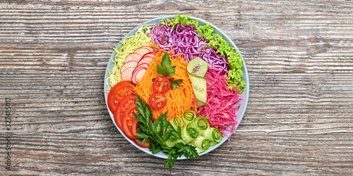 Rainbow salad with tomato, lettuce, cucumber, red cabbage, carrot, radish. Paleo diet, healthy vegan and balanced food concept. Fresh mix green leaves homemade vegetable salad on wood, top view