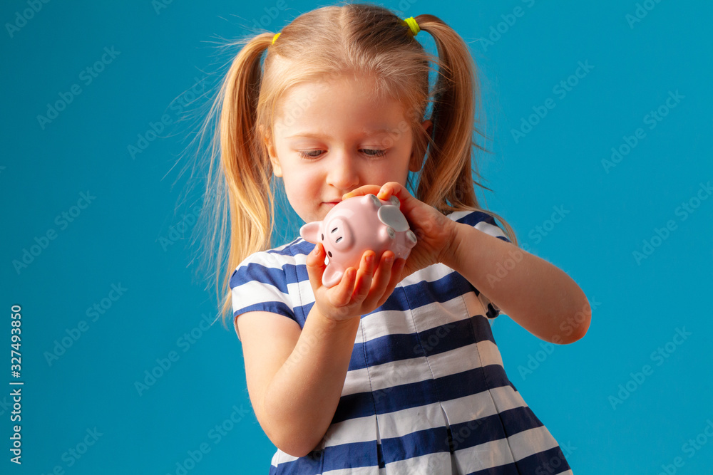 Little girl with piggy bank moneybox against blue background Little girl with piggy bank moneybox against blue background