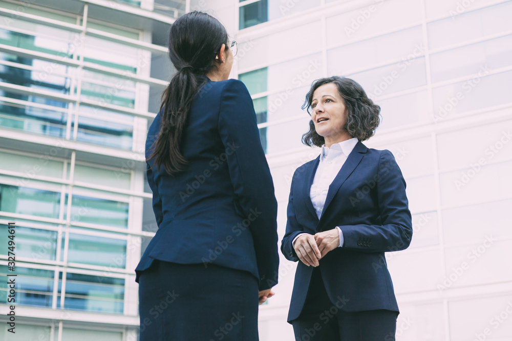 Bottom view of confident colleagues talking on street. Cheerful young confident employees wearing formal suits looking at each other. Business confidence concept Bottom view of confident colleagues talking on street. Cheerful young confident employees wearing formal suits looking at each other. Business confidence concept