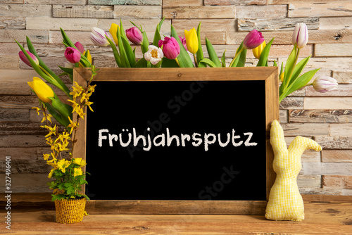 Blackboard With German Text Fruehjahrsputz Means Spring Cleaning. Colorful Tulip Spring Flower Decor. Brick Wall Background photo