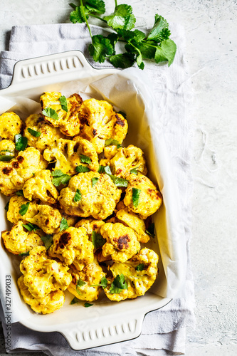 Baked cauliflower with spices and greens in black oven dish.