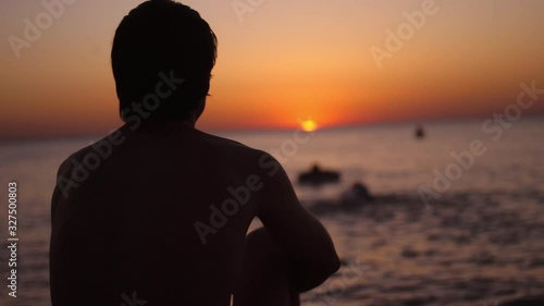 Silhouette of a man sitting alone on the beach looks sunset. Lonely, thinking person.