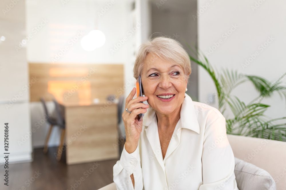 Happy senior woman using mobile phone at home. Smiling cool old woman with white hair sitting on sofa and messaging with smartphone. Beautiful stylish elderly lady talking on cellphone. Happy senior woman using mobile phone at home. Smiling cool old woman with white hair sitting on sofa and messaging with smartphone. Beautiful stylish elderly lady talking on cellphone.