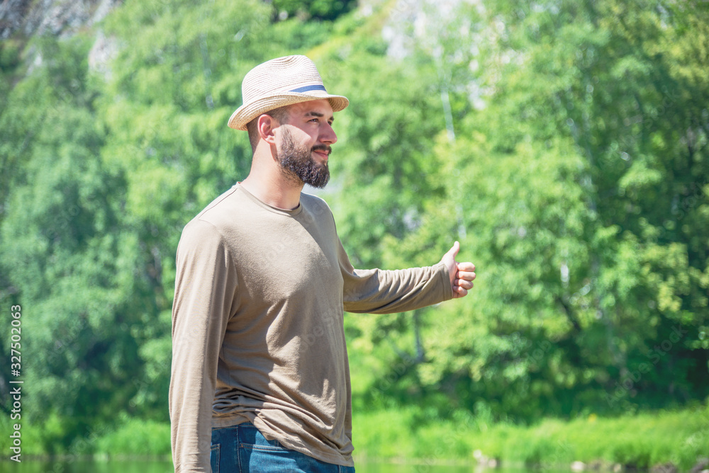 a bearded man in a hat, in a T-shirt and jeans against the background of nature and votes. hitchhiking travel concept