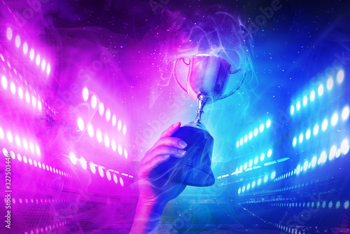 Trophy with smoke effect holding on hand and background blue and violet light for e-sport winner event. © athitat