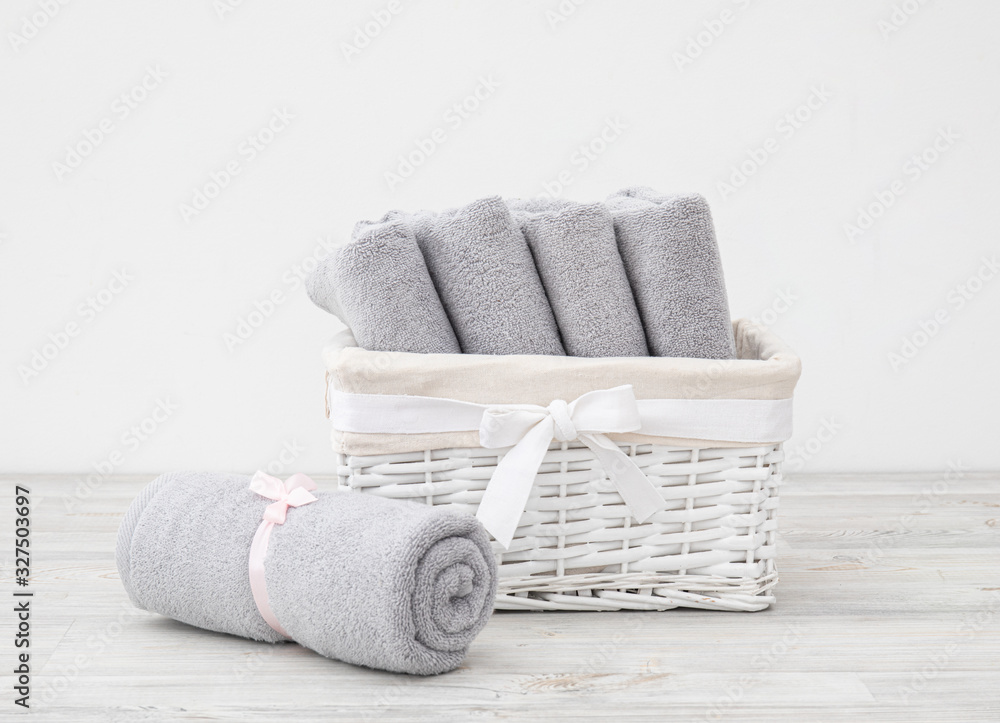 Stack of folded and rolled grey terry towels in the white basket with ribbon on the wooden surface against white background