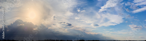 Panorama of the sky with clouds, sun over the trees