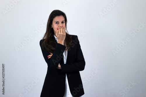 Portrait of scared attractive bussiness woman model feels fear, bits nails, isolated on gray background studio shot, white shirt and black jacket, dark air. Place for your text in copy space.