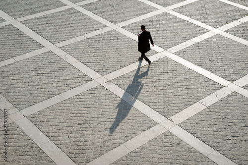 Overhead view of unrecognizable pedestrian casting shadow on the geometric patterns of a stone plaza on a quay next to the River Seine in Paris, France