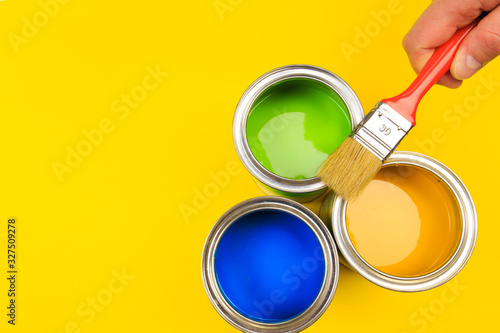 Wallpaper Mural hand holding Brush  on open cans of paint on yellow background. Renovation concept - Image Torontodigital.ca