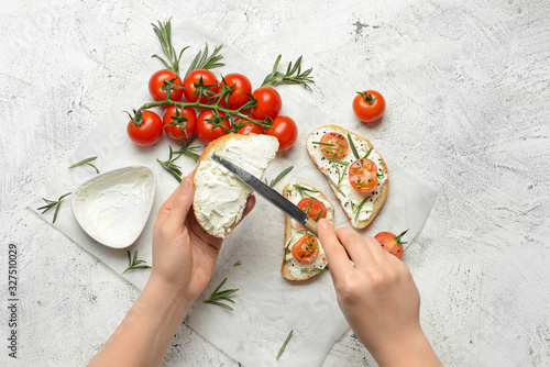 Woman making tasty sandwich with cream cheese on white background