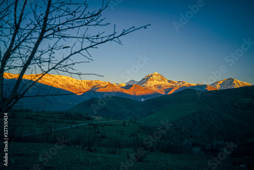 a sunset view of mountains covered with snow in the fall season in  the north of Iraq Kurdistan Region with green landscape and trees in the foreground