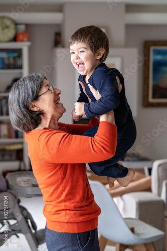Quadro em tela Happy smiling grandmother playing with her little grandson holding him in her arms in the air
