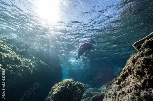 Woman freediver glides with fins. over rocky bottom sea. Freediving and beautiful light in blue sea.