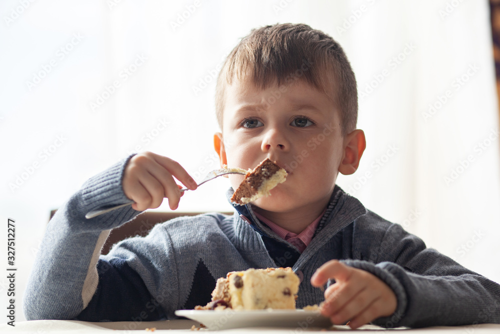 Cute little boy in cafe eat a big piece of cake with a fork. Desserts