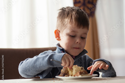 Cute little boy in cafe eat a big piece of cake with a fork. Desserts for kids.