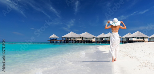 Foto woman wearing white dress and hat walking towards overwater bungalows