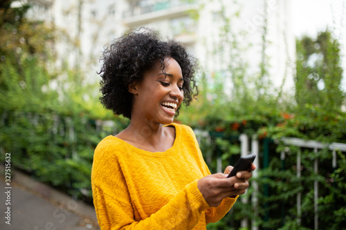 happy young black woman looking at mobile phone outdoors