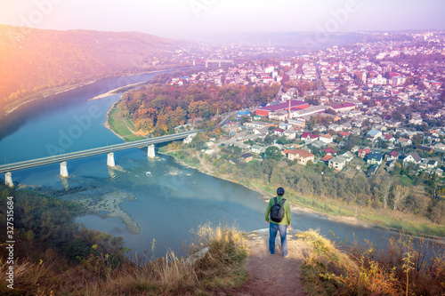 A man stands on a hill and looks at a fantastic view of the winding Dniester River at dawn in the fall. Dniester Canyon National Park, Zalishchyky town, Ternopil region, Ukraine
