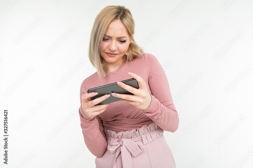 Caucasian blond girl in pink clothes plays on the phone in horizontal format on a white background Caucasian blond girl in pink clothes plays on the phone in horizontal format on a white background