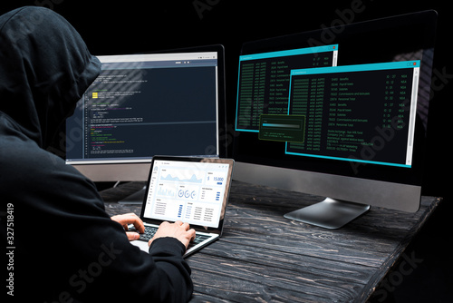 Wallpaper Mural hacker using laptop with charts and graphs on screen near computer monitors on black Torontodigital.ca