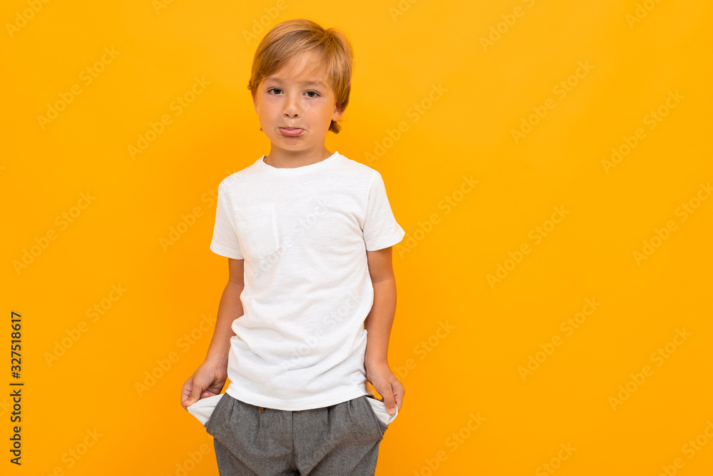 Cute little boy in t-shirt and trousers holds his hands in pockets isolated on yellow background Cute little boy in t-shirt and trousers holds his hands in pockets isolated on yellow background