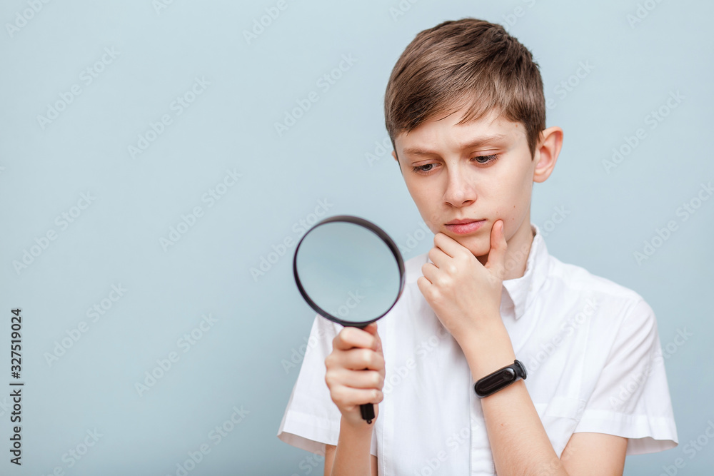 Pensive student young man looks through a magnifying glass. Learning. Isolated on a blue background Pensive student young man looks through a magnifying glass. Learning. Isolated on a blue background