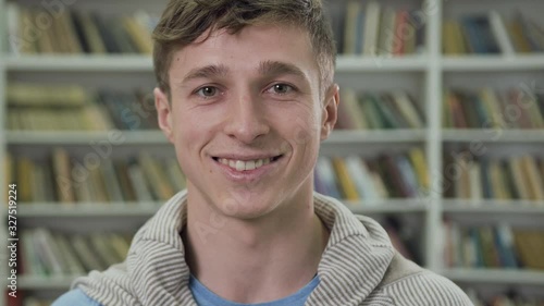 Slow motion of good-looking neat smiling 25-aged man in eyeglasses which posing in library photo