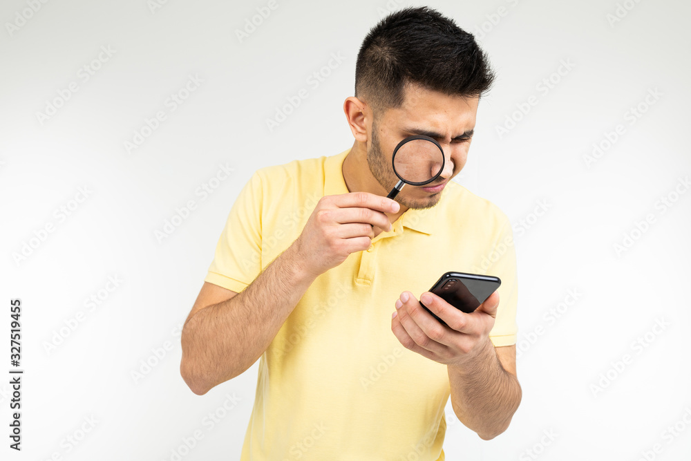 handsome man with myopia holds a magnifier and a smartphone in his hand on a white background with copy space handsome man with myopia holds a magnifier and a smartphone in his hand on a white background with copy space