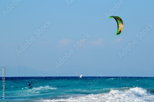 Ixia, Rhodes, Greece. A kiteboarder harnesses the power of the wind with a large controllable power kite to be propelled across the sea water. Pebble beach in Paralia/Ixia