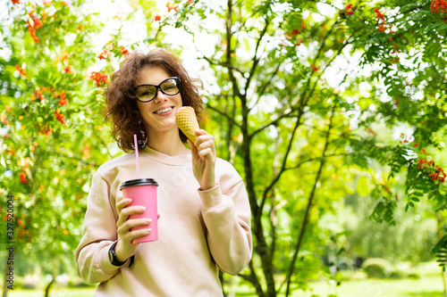 Pretty young caucasian woman go for a walk at park with coffe and ice-cream